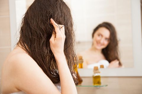 Olivenöl für die Haare: Frau steht vor dem Spiegel und massiert Olivenöl in die Haare ein