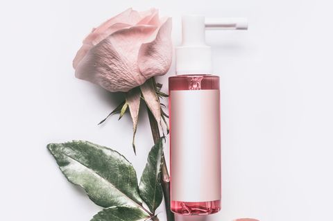 Rosenwasser: Rose auf weißem Tisch und ein Pumpspender mit Rosenöl