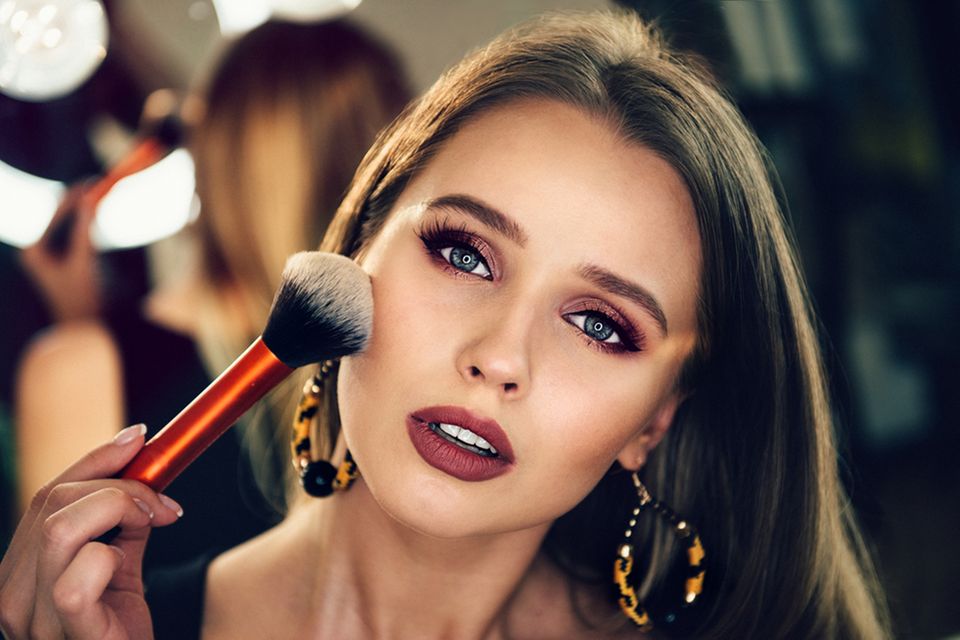 Abend-Make-up: 5 Steps zum perfekten Look: Frau hält sich Schminkpinsel ins Gesicht
