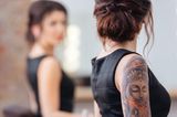 Tattoo am Arm: Frau mit Armtattoo vorm Spiegel