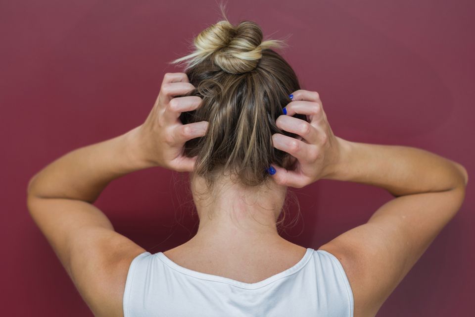 Trockene Kopfhaut: Ursachen und effektive Tipps: Frau fasst sich mit beiden Händen an den Hinterkopf