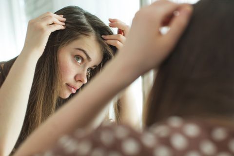 Pickel auf der Kopfhaut: Ursache, Tipps und Behandlung: Frau schaut in den Spiegel und begutachtet ihre Kopfhaut