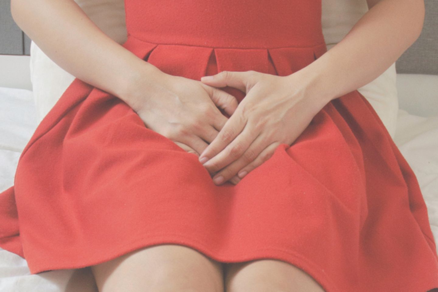 Bakterielle Vaginose: Frau in rotem Kleid fasst sich mit beiden Händen an den Unterleib