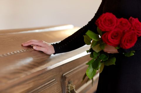 Trauernde Frau legt ihre Hand auf einen Sarg