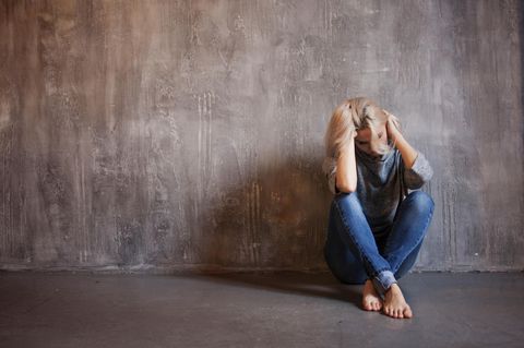 Michaela Muthig: Eine blonde junge Frau sitzt mit gesunkenem Kopf auf dem Boden an eine Wand gelehnt