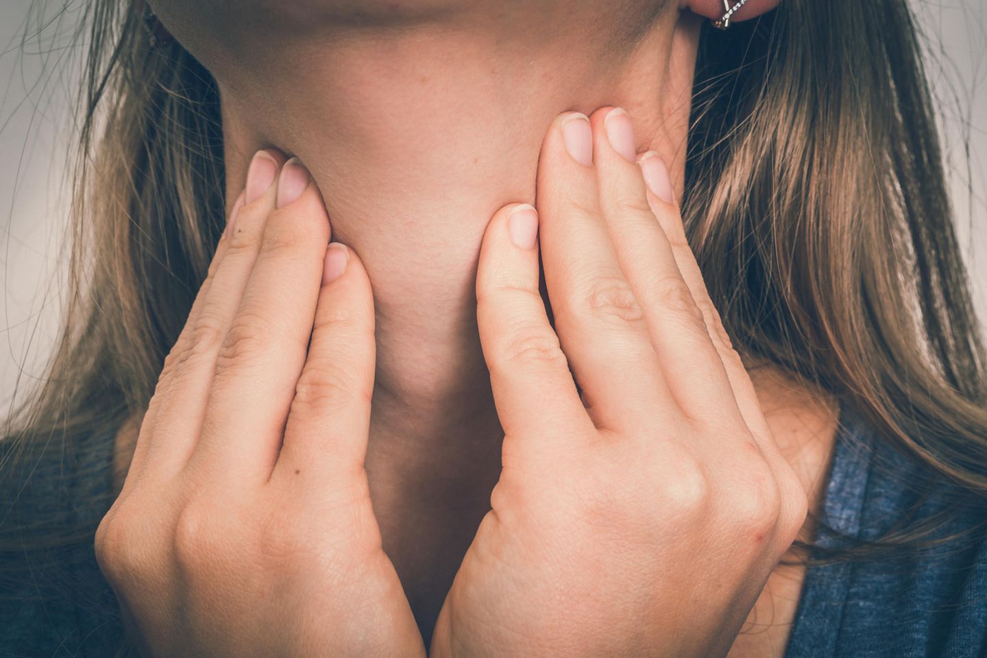 Schilddrüsenüberfunktion: Frau berührt mit beiden Händen ihren Hals