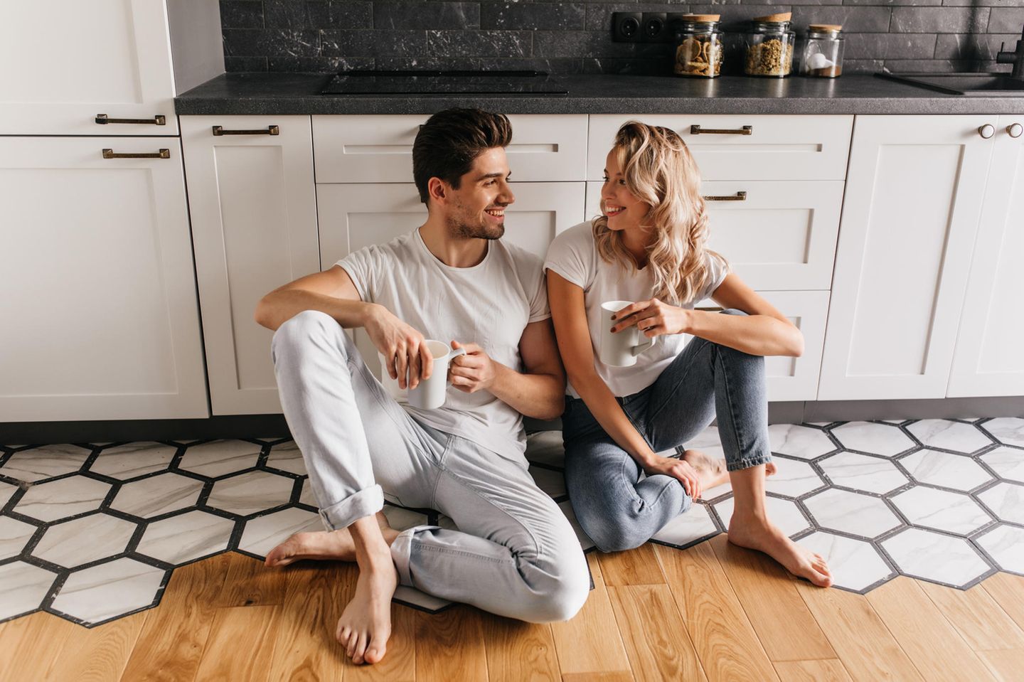 Worüber streiten glückliche Paare? Ein glückliches Paar sitzt in der Küche und schaut sich provokativ lächelnd an