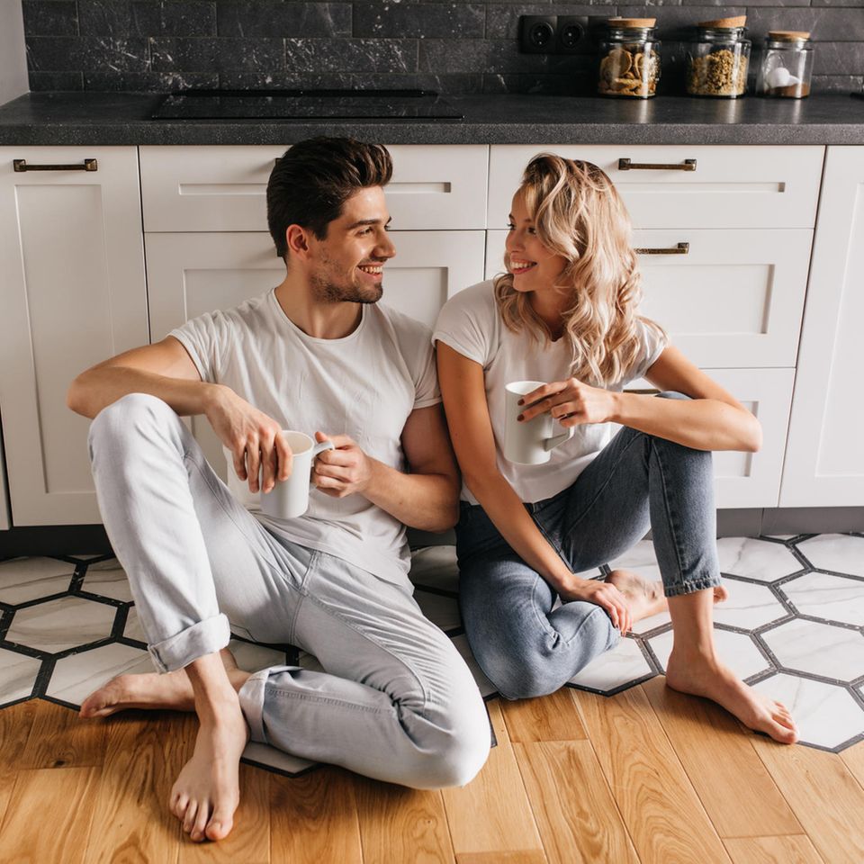 Worüber streiten glückliche Paare? Ein glückliches Paar sitzt in der Küche und schaut sich provokativ lächelnd an