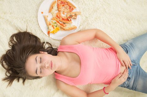 Müdigkeit nach dem Essen: Frau liegt schlafend neben Pizza