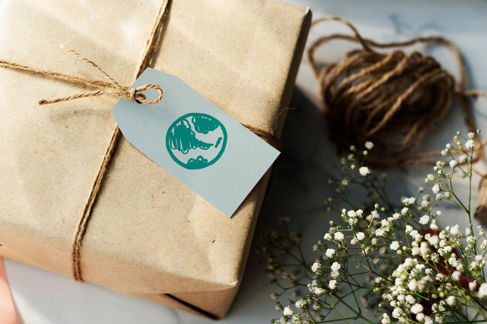 Nachhaltige Geschenke: Geschenk in Packpapier gewickelt, daneben Packband und Schleierkraut