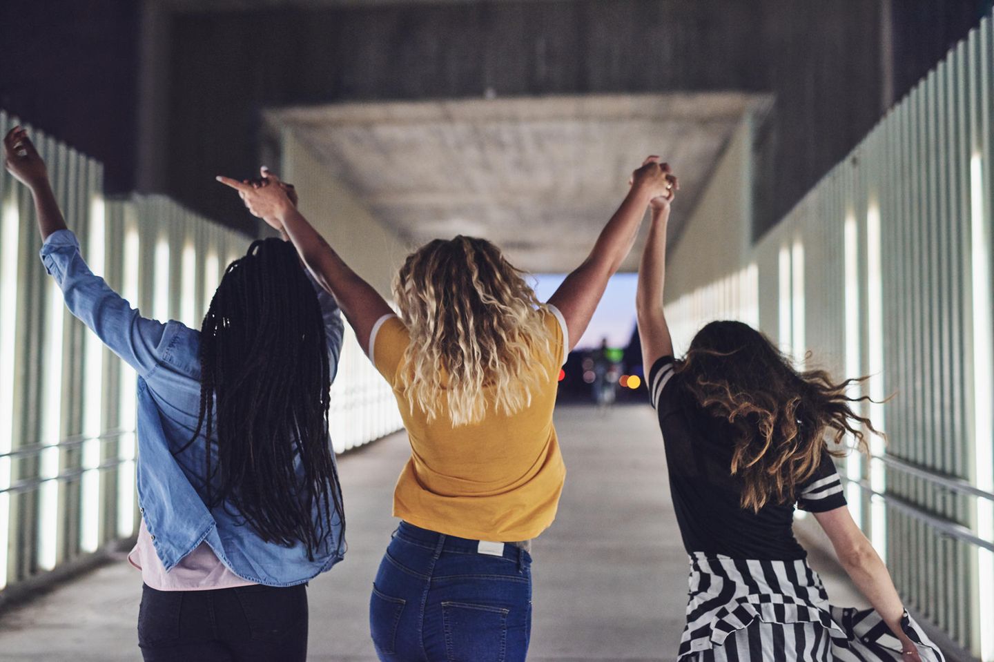 Dinge, die nur selbstbewussten Menschen helfen: Drei Frauen laufen mit hoch gestreckten Händen durch einen Tunnel