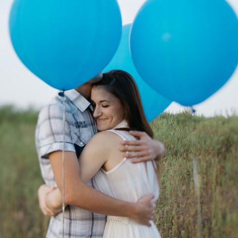 Wie beendet man einen unnötigen Streit? Ein Pärchen umarmt sich umgeben von blauen Luftballons