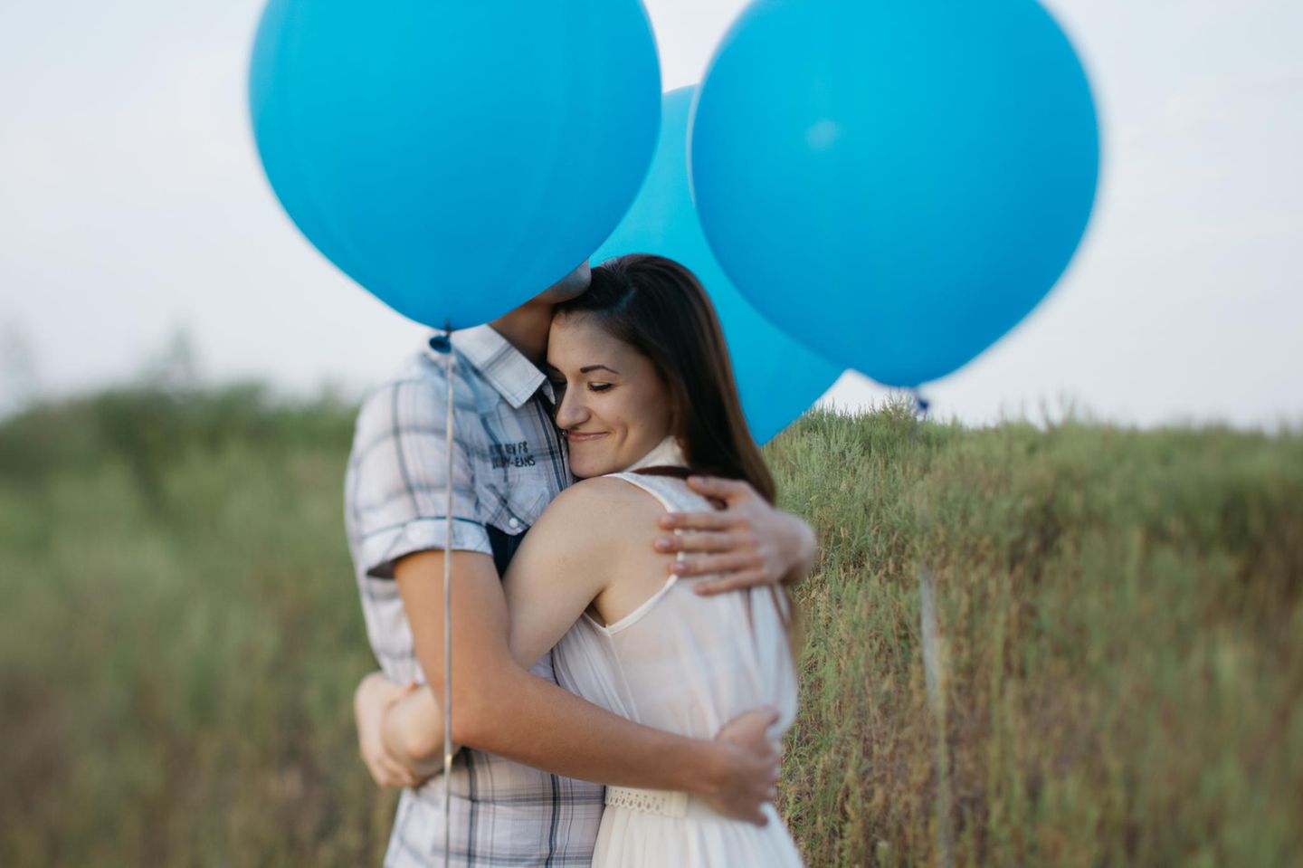 Wie beendet man einen unnötigen Streit? Ein Pärchen umarmt sich umgeben von blauen Luftballons