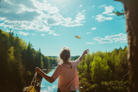 Was ist Glück? Eine junge Frau am Fluss wirft einen Papierflieger in die Luft