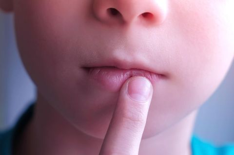 Herpes im Mund: Junge legt Zeigefinger auf die Lippen