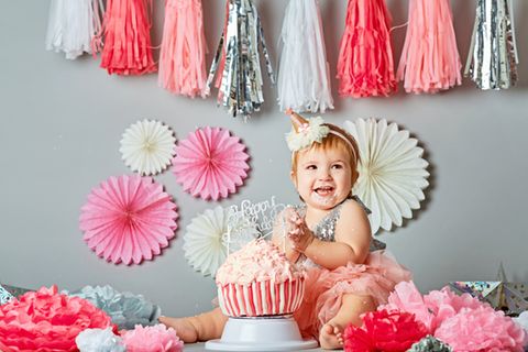 Geschenke zum 1. Geburtstag: Kleinkind sitzt vor Geburtstagskuchen und lacht