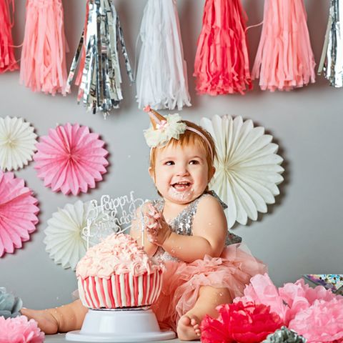 Geschenke zum 1. Geburtstag: Kleinkind sitzt vor Geburtstagskuchen und lacht