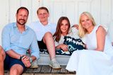 Mette-Marit und Prinz Haakon sitzen mit ihren Kindern vor einem Haus
