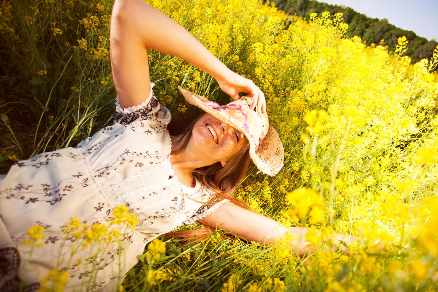 Erdzeichen: Eine Frau mit Hut liegt auf einer gelben Blumenwiese
