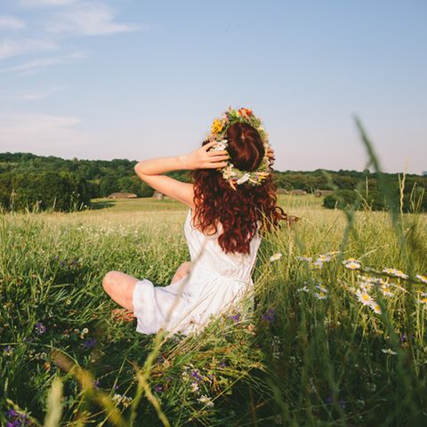 Blumenkranz selber machen: Frau sitzt auf einer Wiese und trägt einen Blumenkranz
