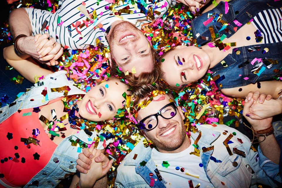Partyspiele: 4 Freunde liegen auf dem Boden nebeneinander mit Konfetti übersät