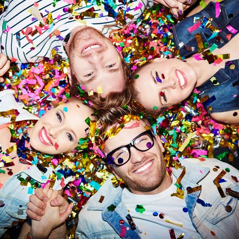 Partyspiele: 4 Freunde liegen auf dem Boden nebeneinander mit Konfetti übersät