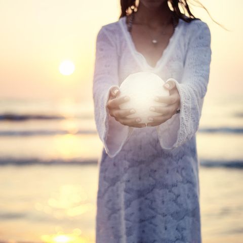 Mondzeichen: Eine Frau steht am Meer und hält einen kleinen Mond in den Händen