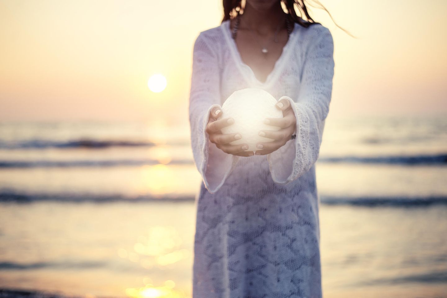 Mondzeichen: Eine Frau steht am Meer und hält einen kleinen Mond in den Händen