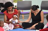 Herzogin Meghan+ Prinz Harry in Afrika: Meghan Markle sitzt auf dem Boden und berührt ein Baby
