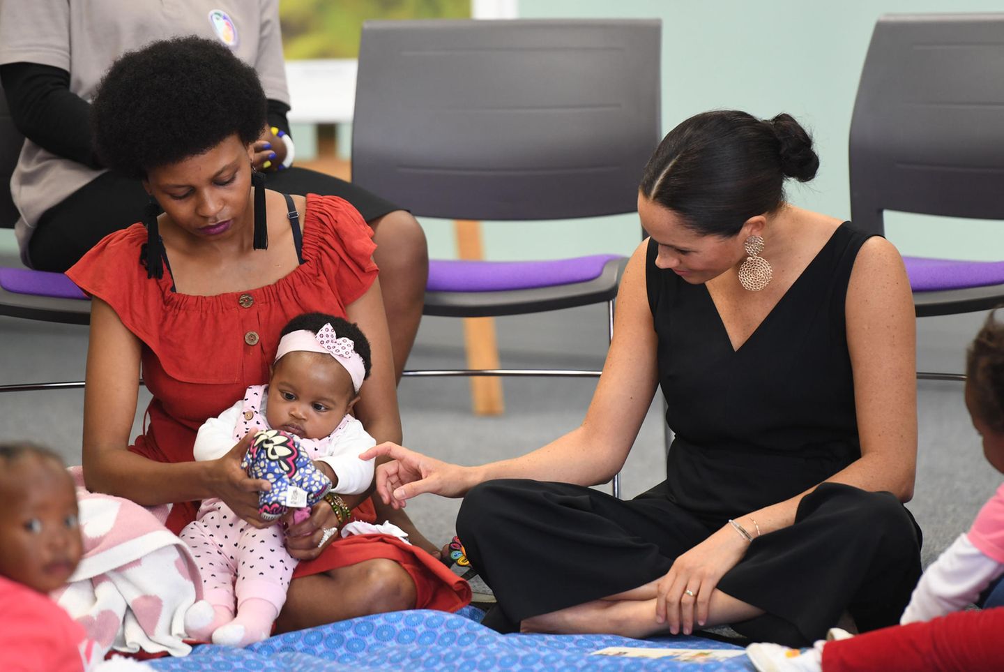 Herzogin Meghan+  Prinz Harry in Afrika: Meghan Markle sitzt auf dem Boden und berührt ein Baby