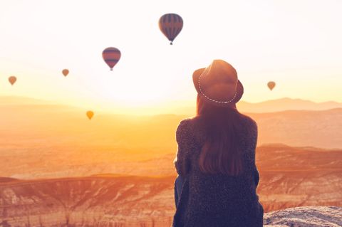 Horoskop: Eine Frau sitzt auf einem Hügel und beobachtet Heißluftballons