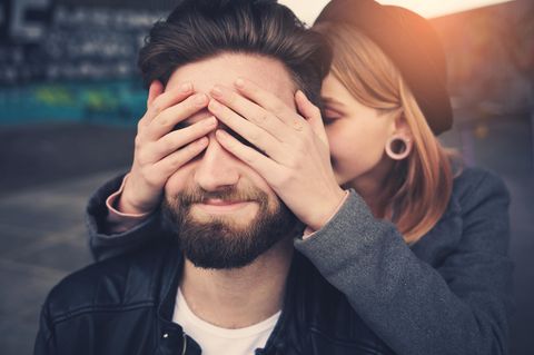 Reddit: Eine Frau hält einem Mann die Augen zu und flüstert ihm etwas ins Ohr