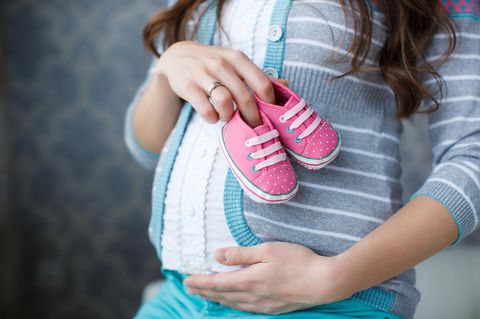 Fruchtbarkeit: Schwangere Frau hält Kinderschuhe