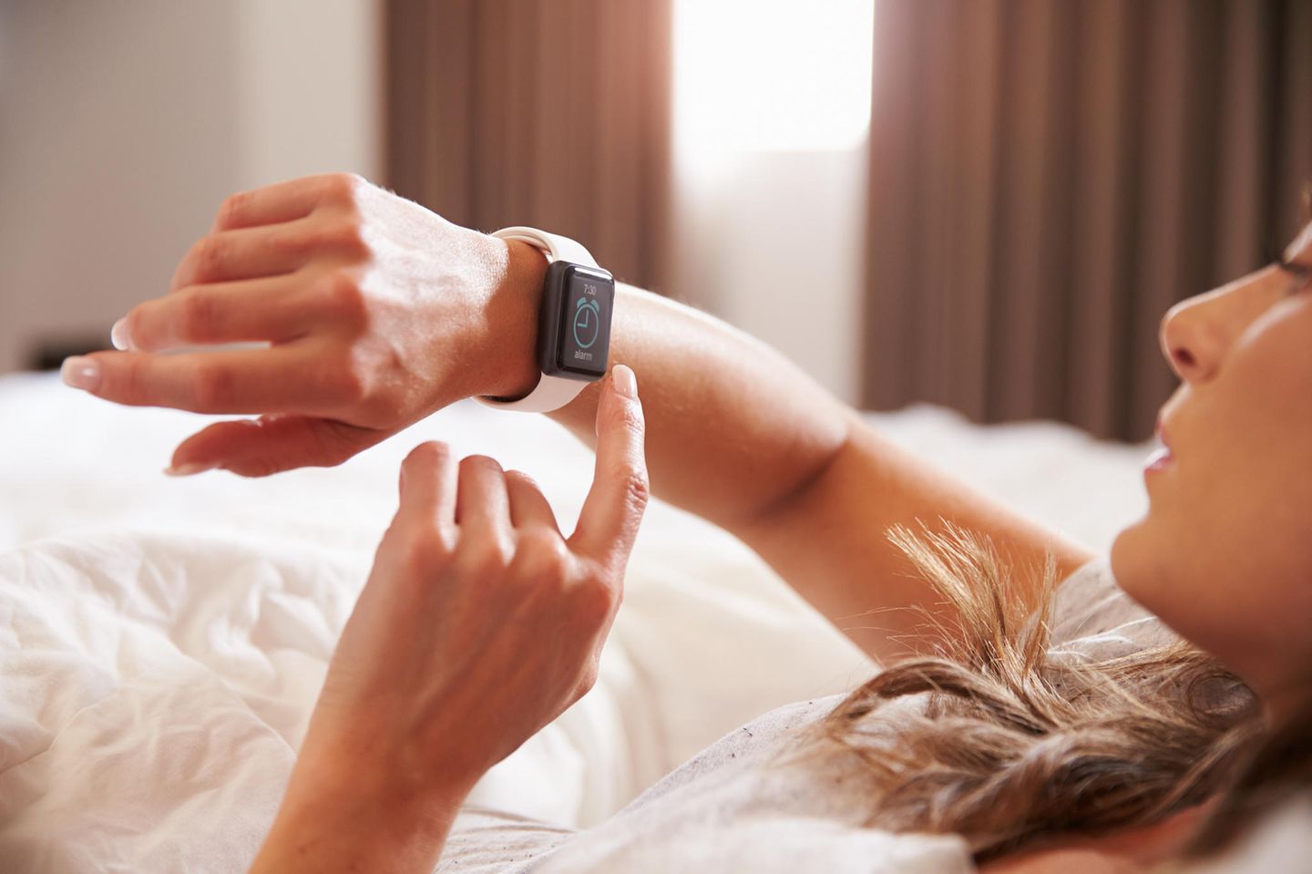 Uhrzeiten-Bedeutung: Eine Frau liegt im Bett schaut auf ihre Armbanduhr