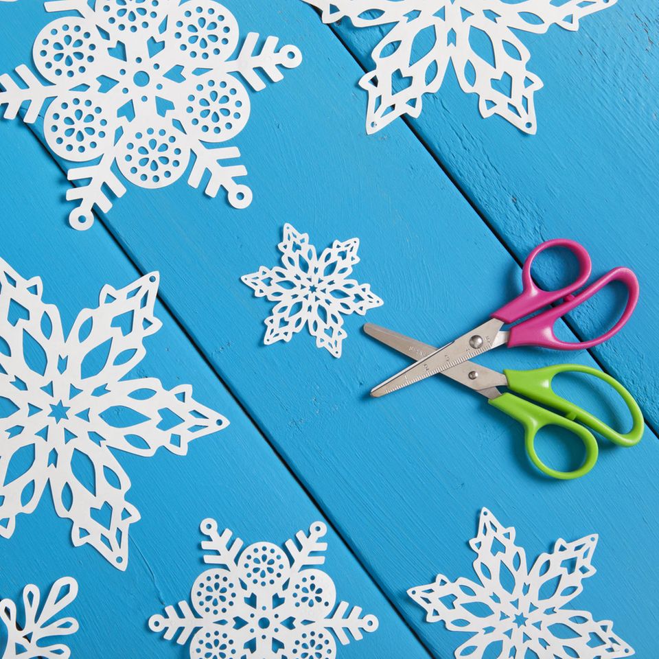 Bastelideen Winter: Papierschneeflocken auf blauem Untergrund