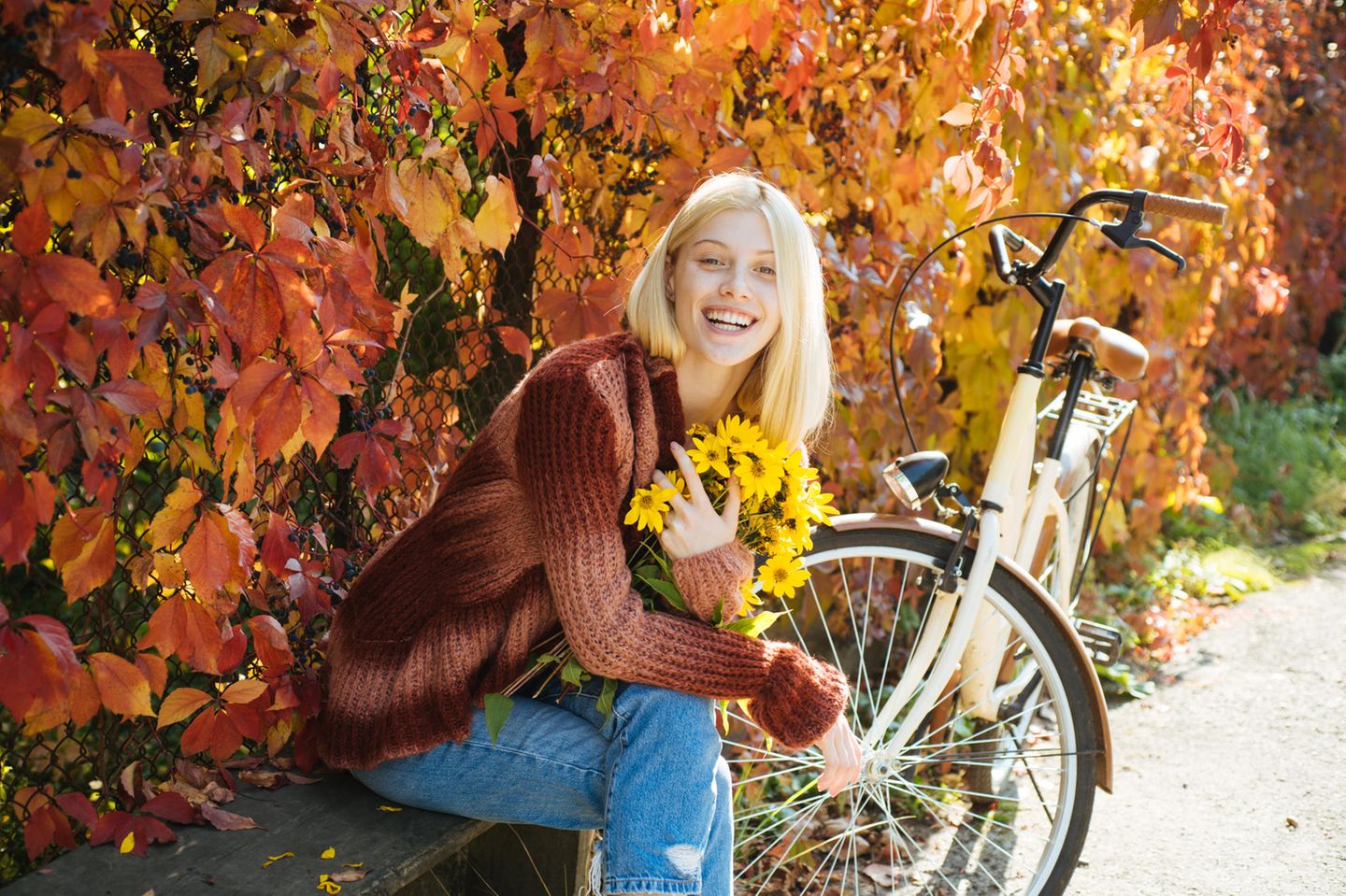 Horoskop: Eine glückliche Frau vor einer Herbsthecke mit Sonnenblumen in der Hand