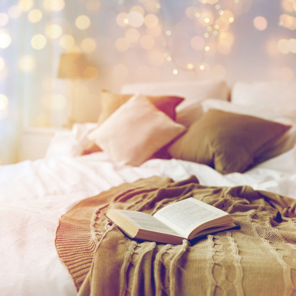 Lichterketten: Buch liegt auf einem Bett, darüber leuchtet eine Lichterkette