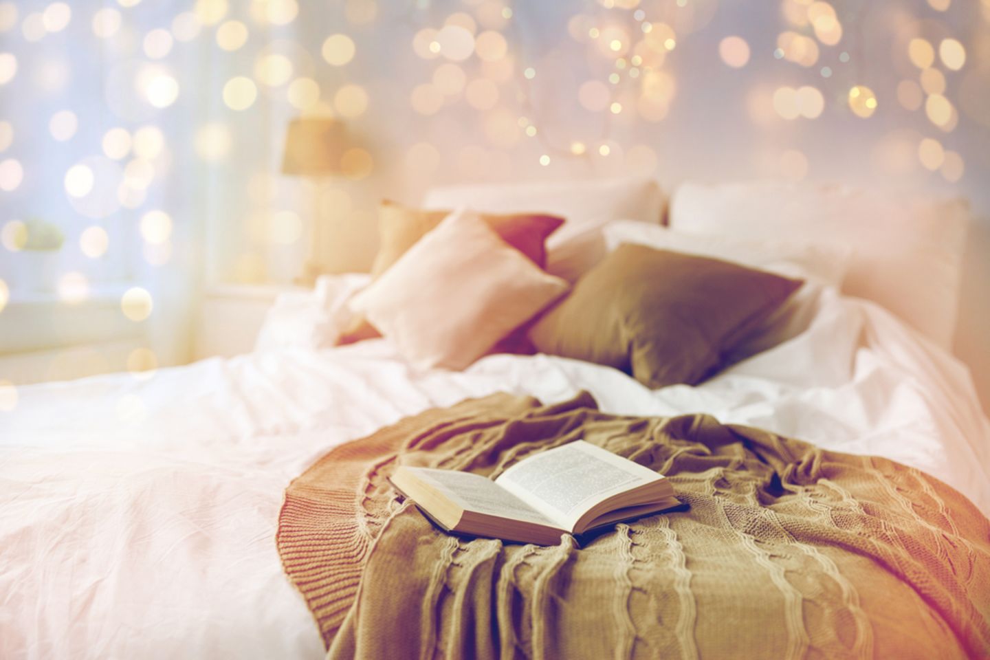 Lichterketten: Buch liegt auf einem Bett, darüber leuchtet eine Lichterkette