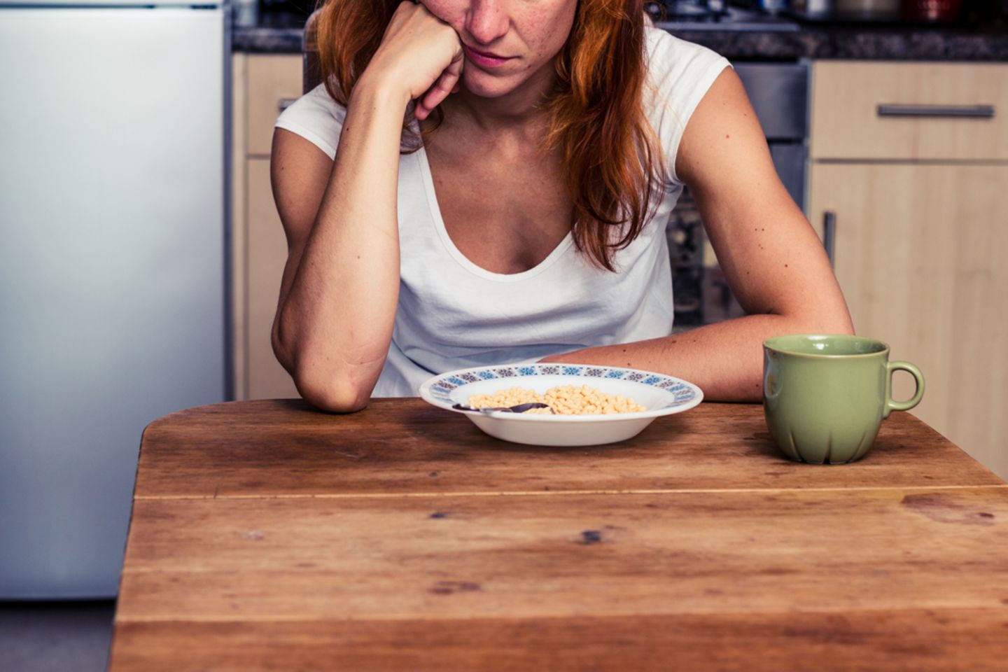 Appetitlosigkeit: Frau sitzt am Esstisch und schaut gelangweilt aufs Essen