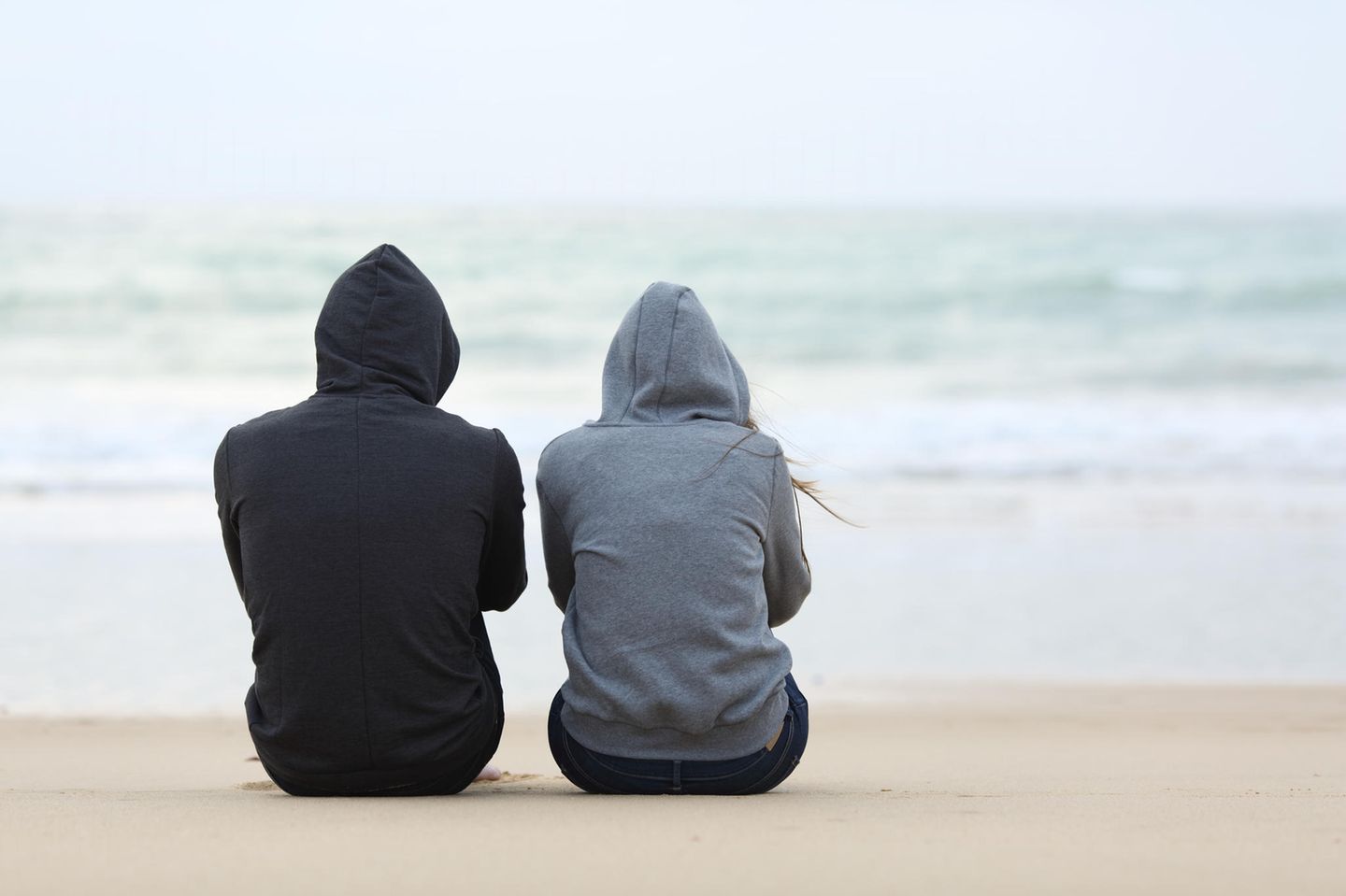 Beziehungskrise: Ein Paar sitzt nebeneinander, ohne sich zu berühren, am Meer
