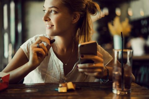 WhatsApp-Nachrichten, die man dem Partner gerne verheimlichen darf: Eine Frau in einer Bar mit einem Handy in der Hand
