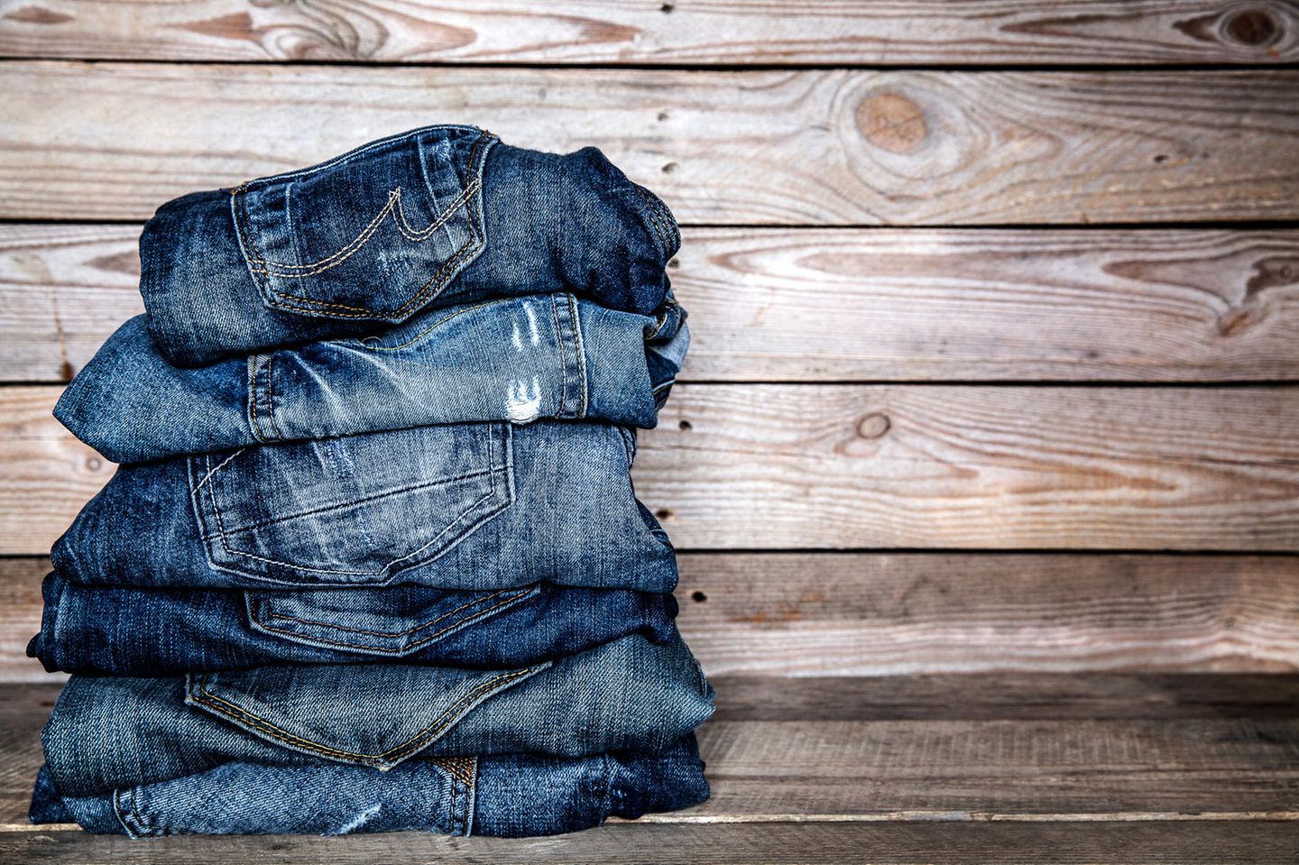 Jeans färben: Jeans in unterschiedlichen Blautönen vor Holzwand