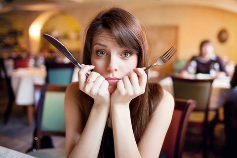 Emotionales Essen: Frau hält Besteck in den Händen und schaut erschrocken