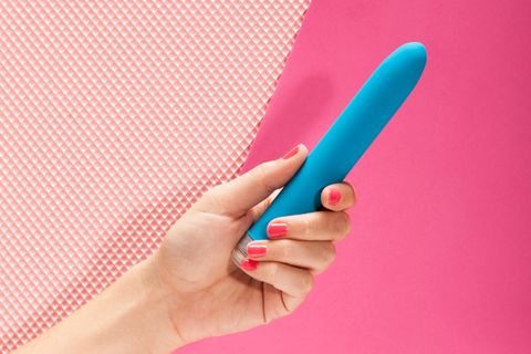 Vibrator vor pinkem Hintergrund in Frauenhand