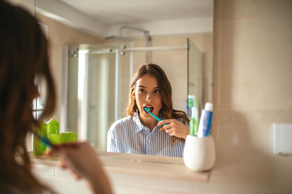 Frau putzt Zähne im Spiegel