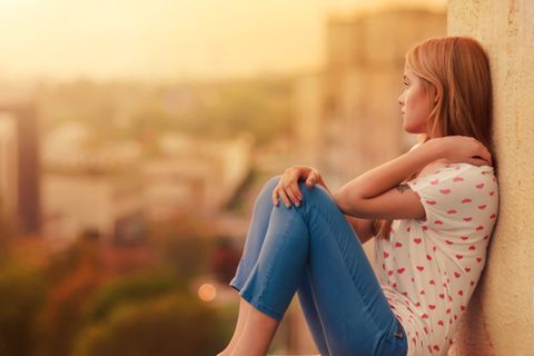Heimweh: Junge Frau sitzt auf Balkon beim Sonnenuntergan