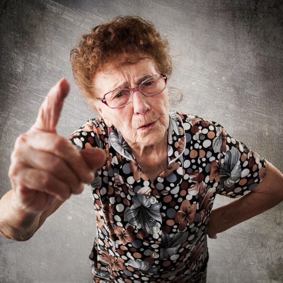 Ältere Frau hebt den Finger in Richtung der Kamera