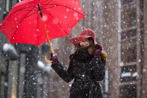 Neujahrsvorsätze, die dich glücklicher machen: Eine fröhliche Frau mit Regenschirm im Schnee