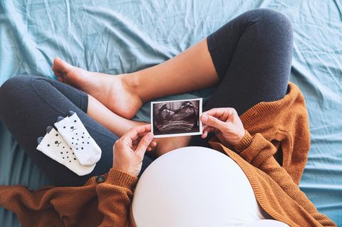 Schwangere Frau auf Bett schaut sich Ultraschallbild an