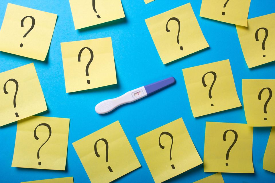 Schwangerschaftstest umgeben von Fragezeichen